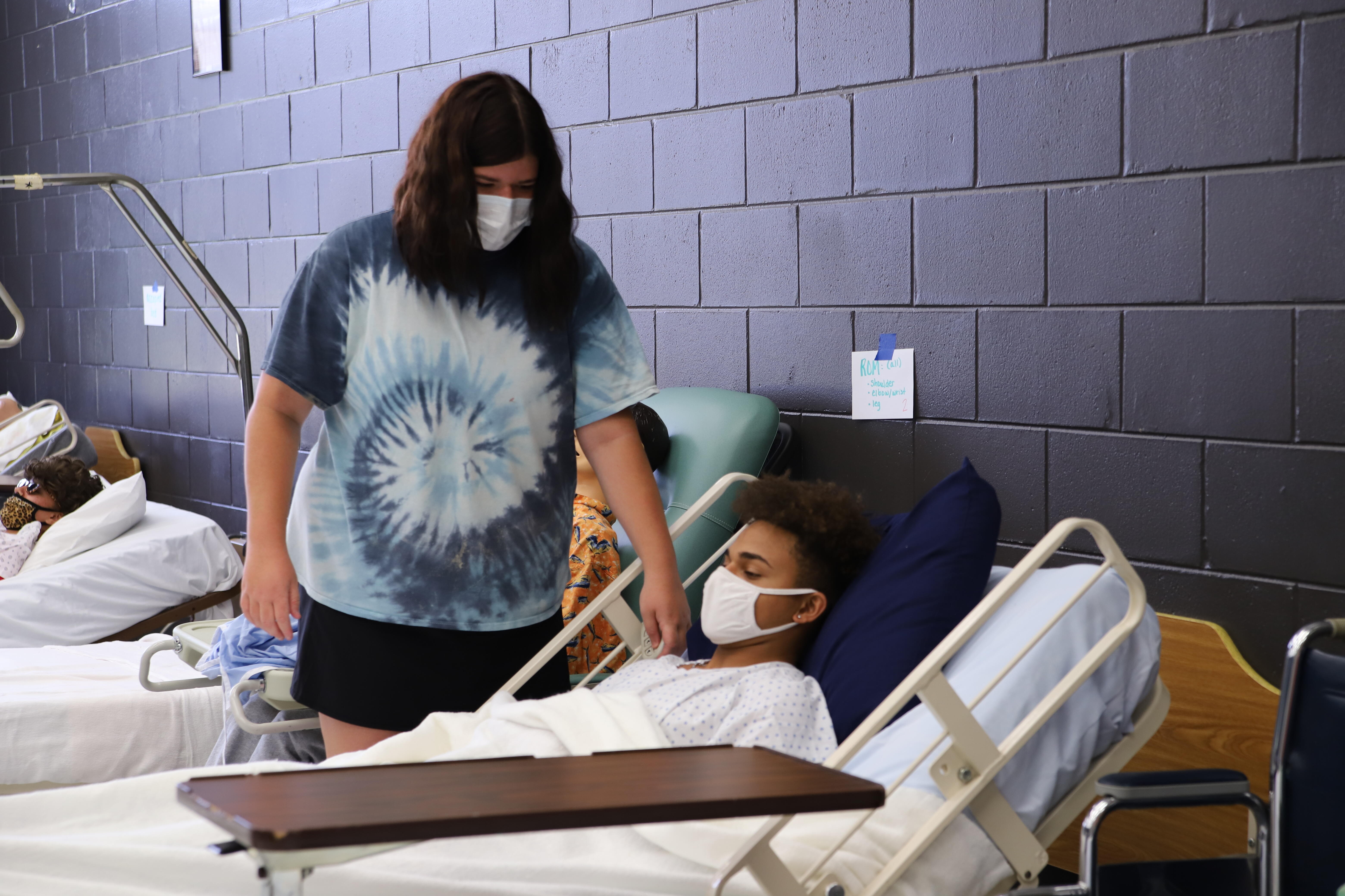 Student in nursing program checking on a student in a hospital bed